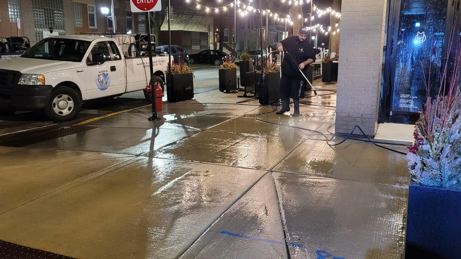 The Lara's Power Wash LLC crew pressure washing a restaurant patio at night, with the company truck parked alongside