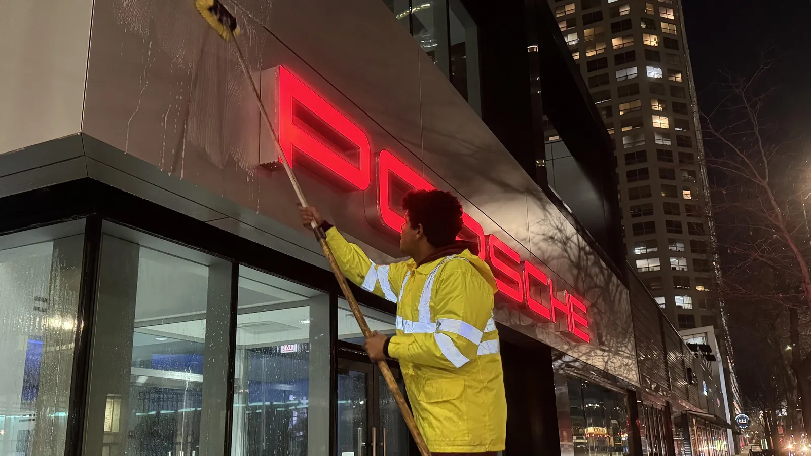 A Lara's Power Wash LLC technician washing a storefront sign and windows at night